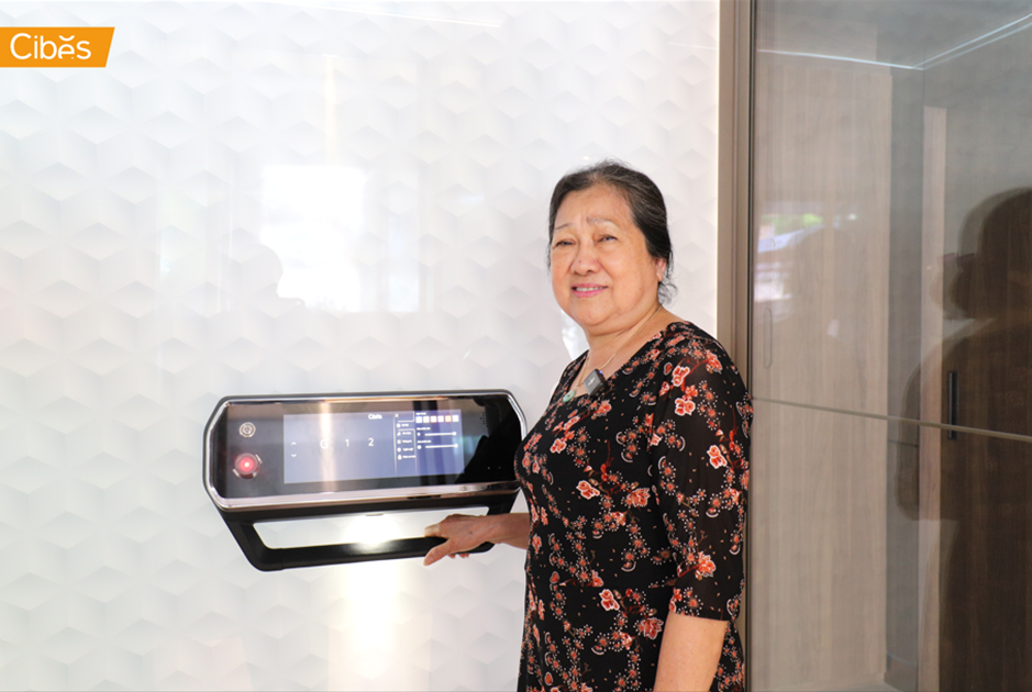 Older woman standing beside a home elevator in a bright modern interior, showing easy and accessible cabin design.