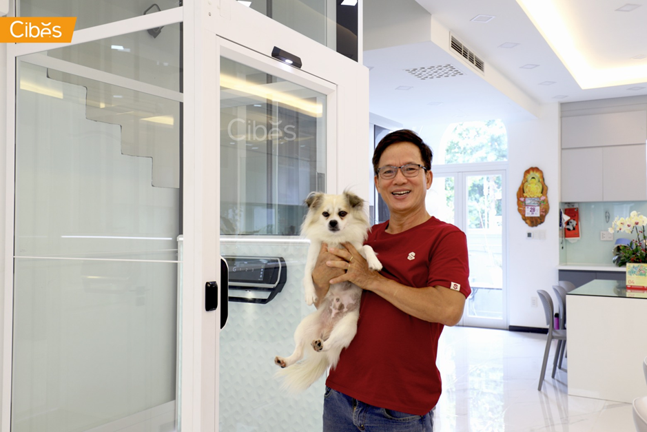 Man holding a small dog beside a home elevator in a modern house interior.