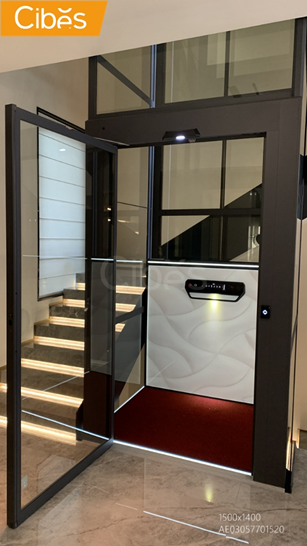 Home elevator with glass and black frame installed in an existing house beside a staircase.